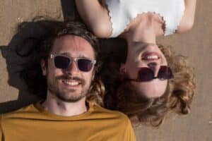 man and woman laughing on the beach wearing sunglasses