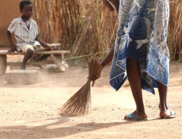 Woman sweeping a clay floor with a straw broom in Ghana Africa.